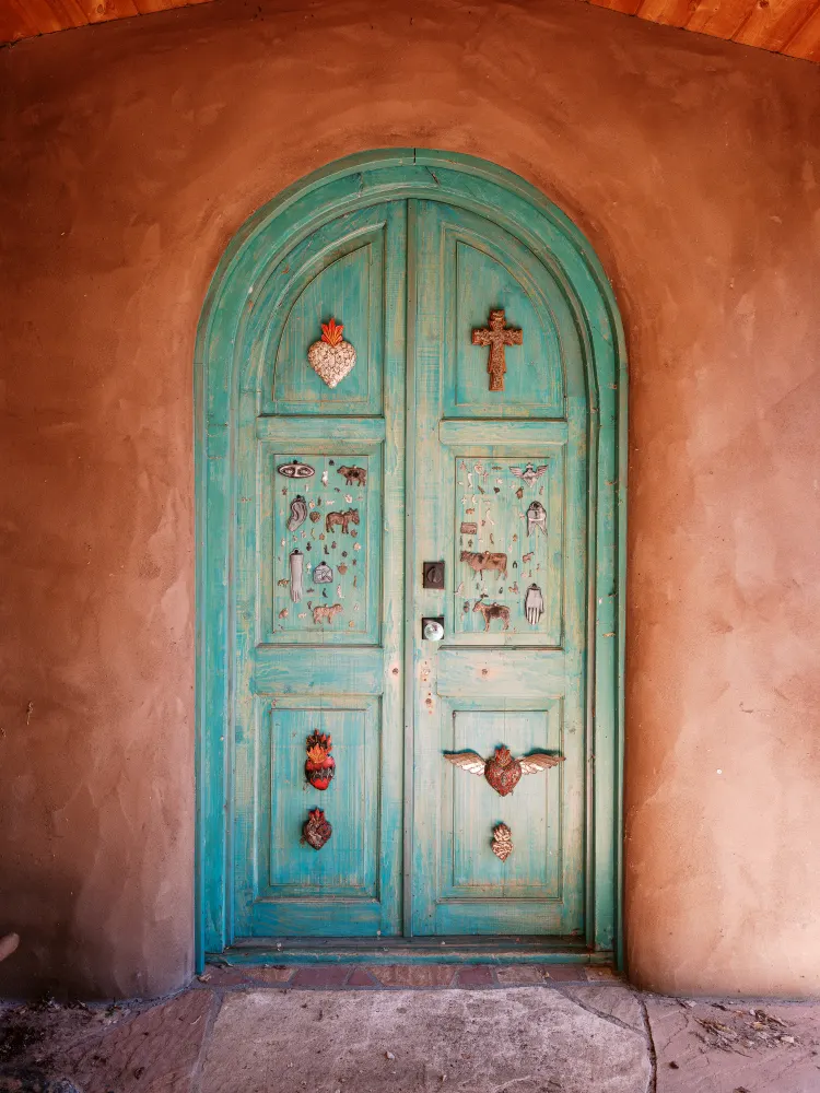 A turquoise door hung with milagros, set in an adobe wall